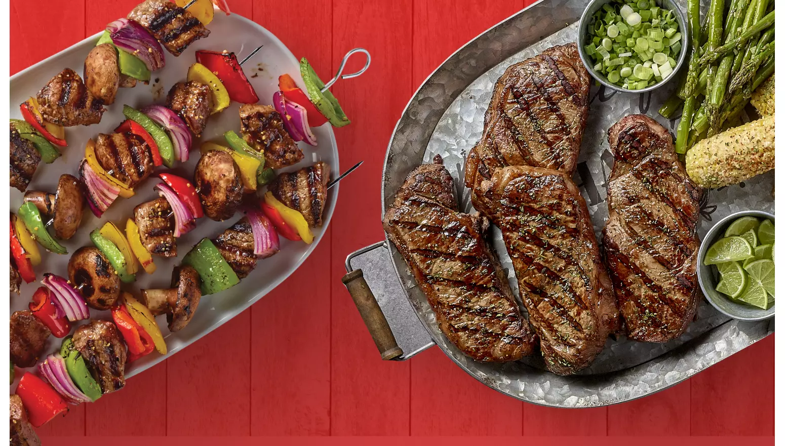A plate of steak kabobs and steaks with corn, asparagus, lime, and chopped green onions