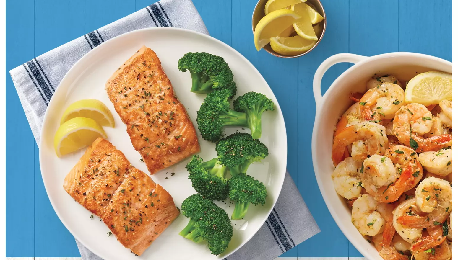 A plate with salmon, lemons, and broccoli; a bowl of shrimp and lemon