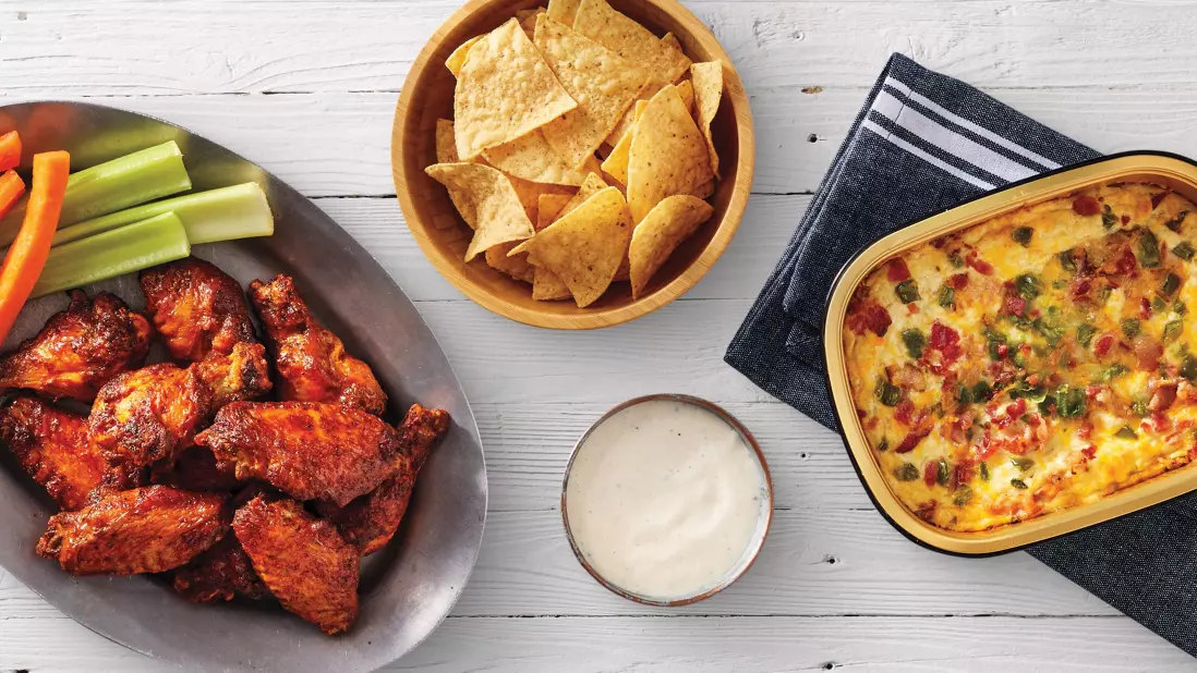  Baked chicken wings with celery and carrot sticks, tortilla chips, a creamy dip, and a hot cheesy dip with jalapeños and red bell peppers.