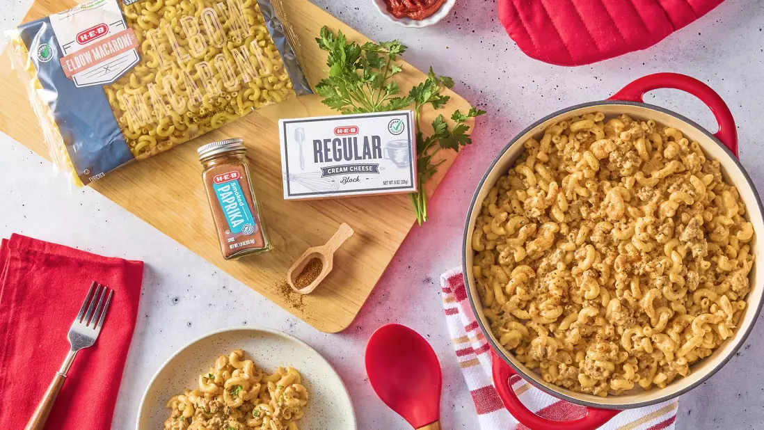 H‑E‑B Elbow Macaroni, Paprika, and Cream Cheese next to a pot and plate of prepared creamy pasta with meat.