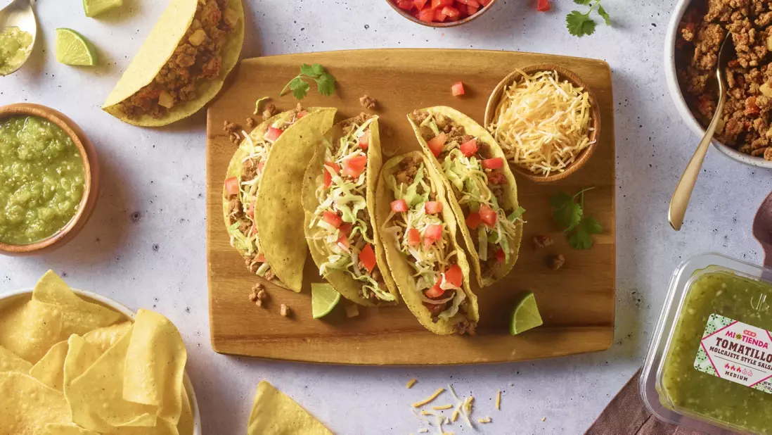 Tacos made and laid on a cutting board, with tomatillo sauce next to it