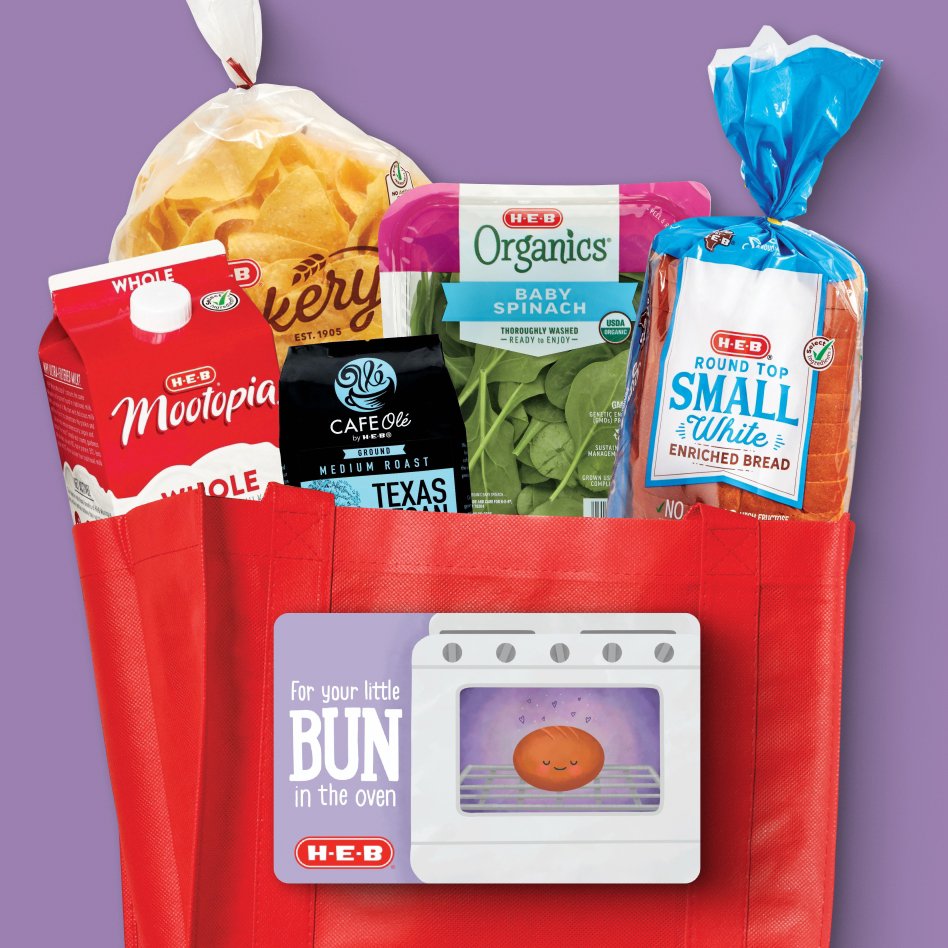 A red H‑E‑B grocery bag filled with various H‑E‑B products, including Mootopia whole milk, H‑E‑B Bakery chips, H‑E‑B Organics baby spinach, Round Top Small White Enriched Bread, and Café Olé Texas Pecan medium roast coffee.