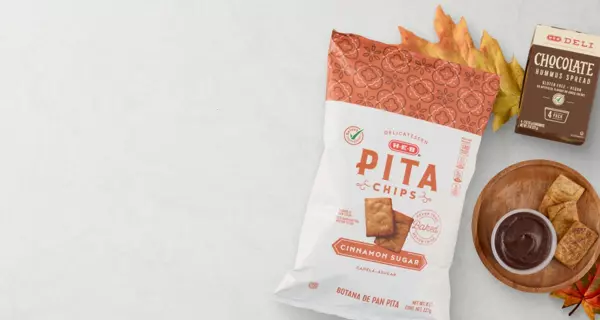 Bag of Stacy's Simply Naked Pita Chips served with chocolate dip and cinnamon sugar pita chips on a light background. Text reads, “A snack for every craving.” Chocolate squares and autumn leaves complete the snack-themed display.