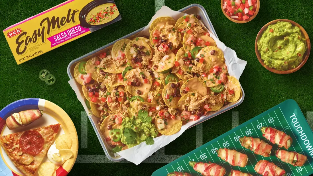 Loaded nachos covered with queso, shredded meat, black beans, jalapeños, tomatoes, and guacamole, displayed alongside H‑E‑B Easy Melt Salsa Queso, guacamole, pico de gallo, pizza, chips, and bacon-wrapped appetizers.