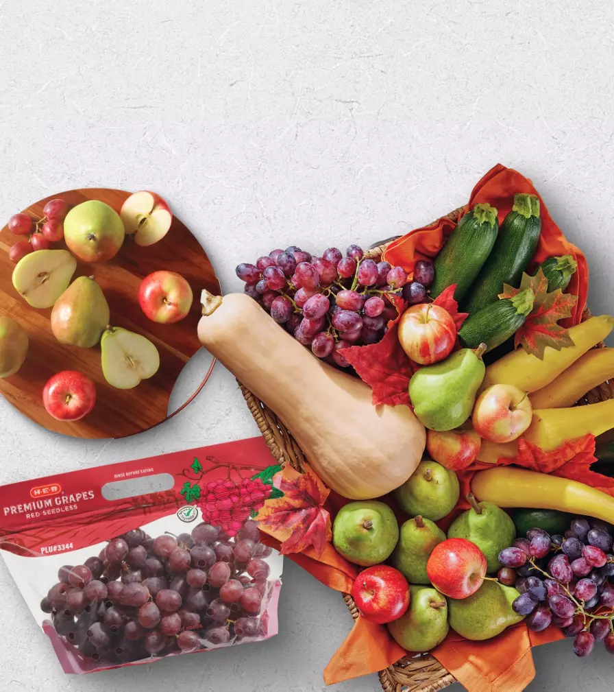Fall produce display featuring red grapes in a bag, pears, apples, squash, zucchini, and decorative autumn leaves. Text reads “Fall’s fresh picks” with the subheading “Crisp, colorful, and full of flavor.” A button appears on the left side of the banner.