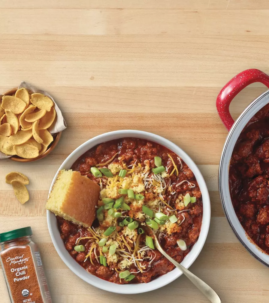 Banner promoting chili night featuring a bowl of chili topped with shredded cheese and green onions, served with cornbread, alongside a pot of chili and ingredients on a wooden countertop. Text reads: “Make it a chili night. All you need for a satisfying meal.” with a “Shop now” button.