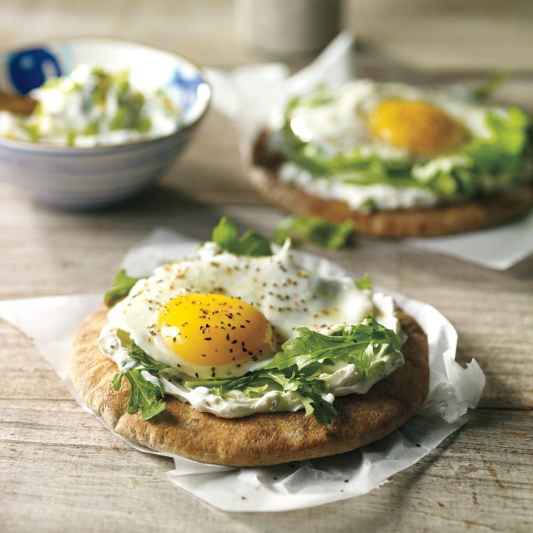 Pita bread topped with cream cheese, a sunny side up egg, chives, and spinach.