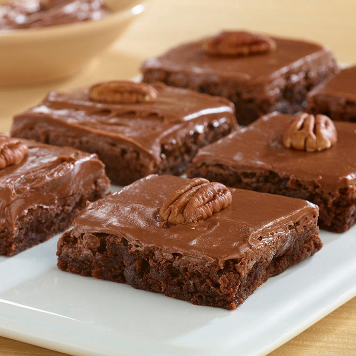 Iced chocolate brownies sliced into squares and topped with pecan halves