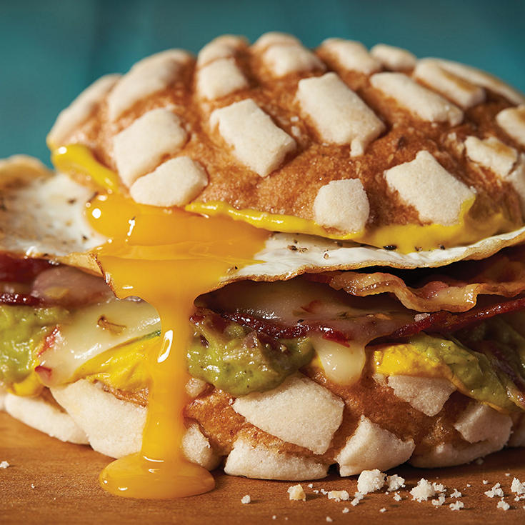 Large concha pastry sandwich made with a fried egg, guacamole, melted pepper jack cheese, and bacon. 