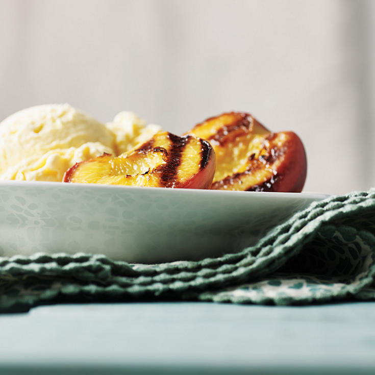 Grilled peach halves in a bowl with vanilla ice cream