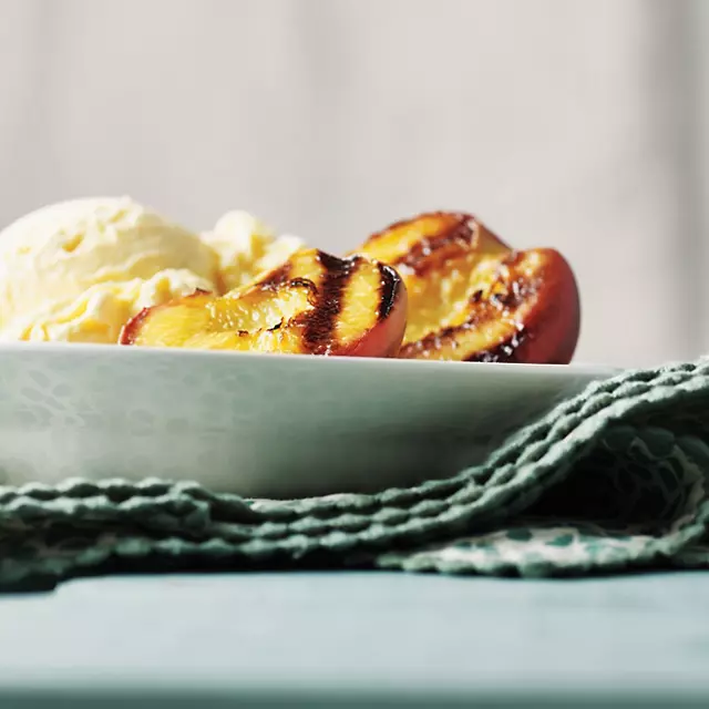 Grilled peach halves in a bowl with vanilla ice cream