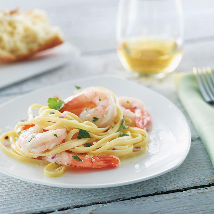 Linguini noodles on a plate topped with shrimp and served with white wine and bread